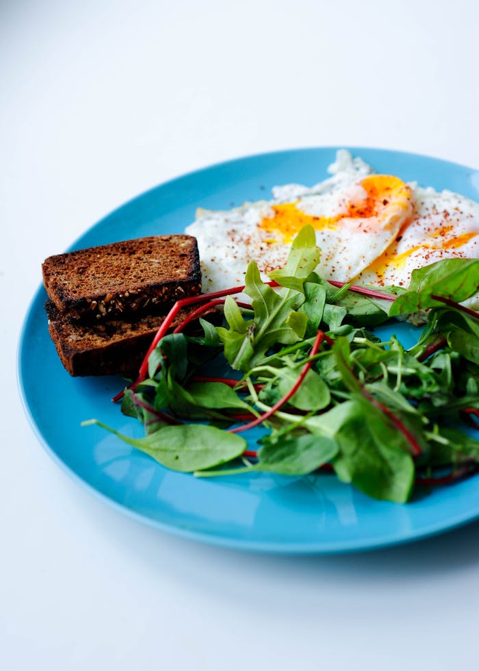 Delicious breakfast featuring fried eggs, toast, and fresh greens served on a vibrant blue plate.