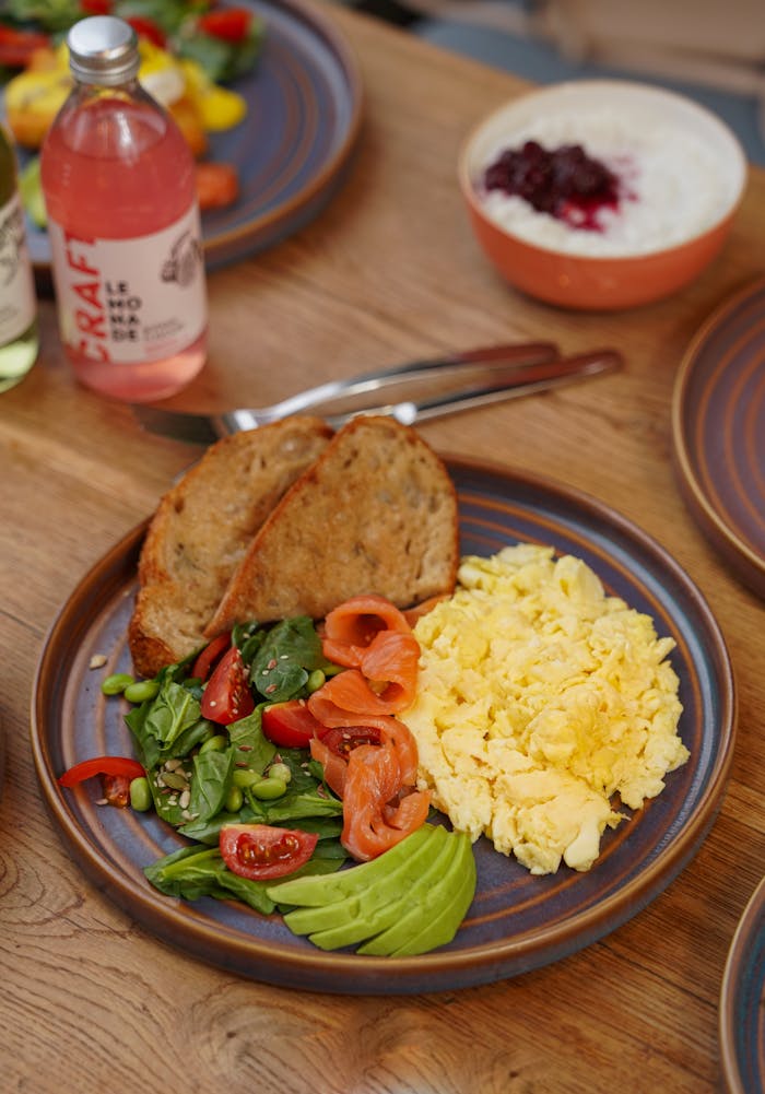 Delicious breakfast plate with scrambled eggs, avocado, and salad on a wooden table.